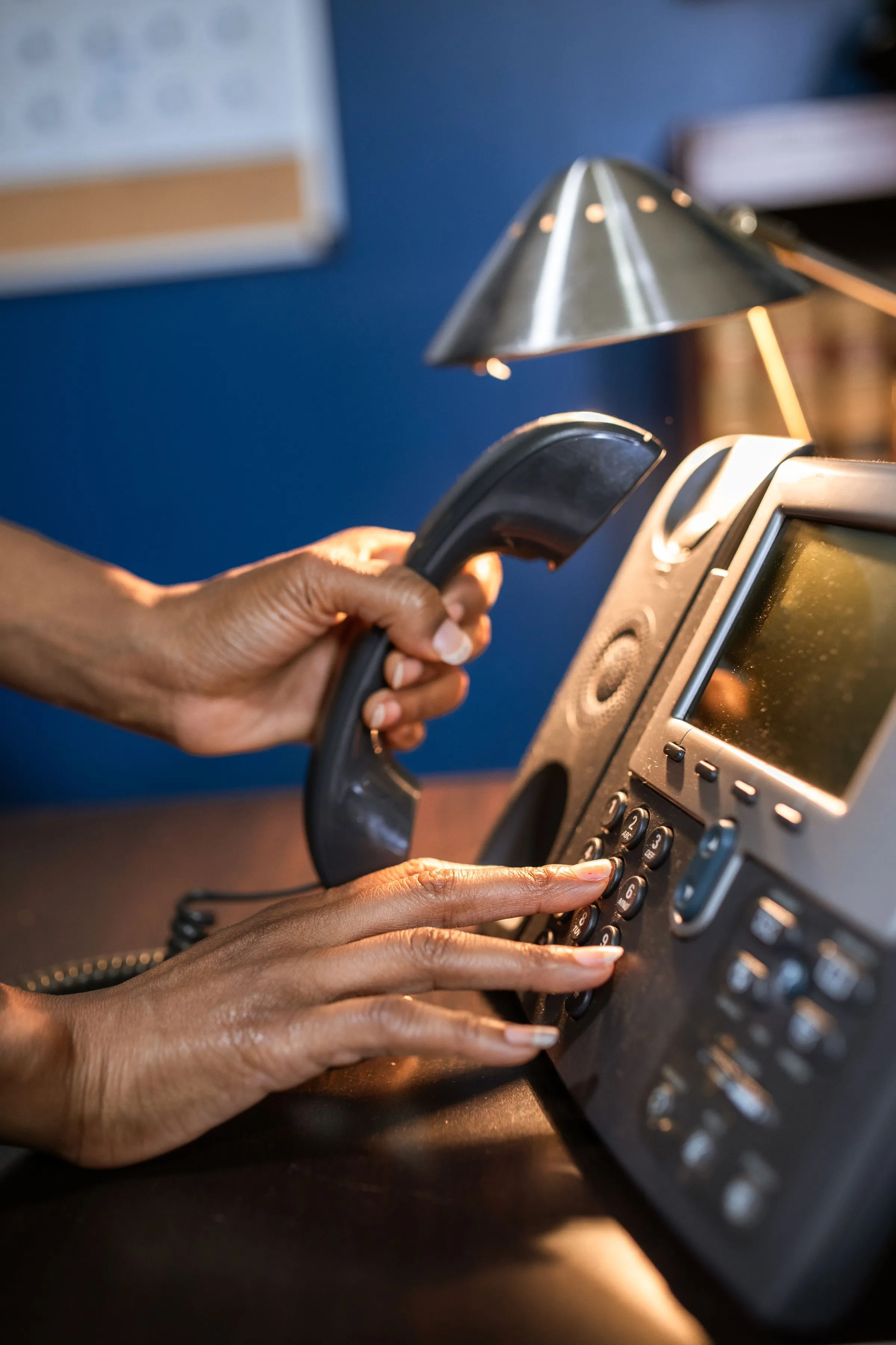 Hands dialling a desk phone with the handset lifted