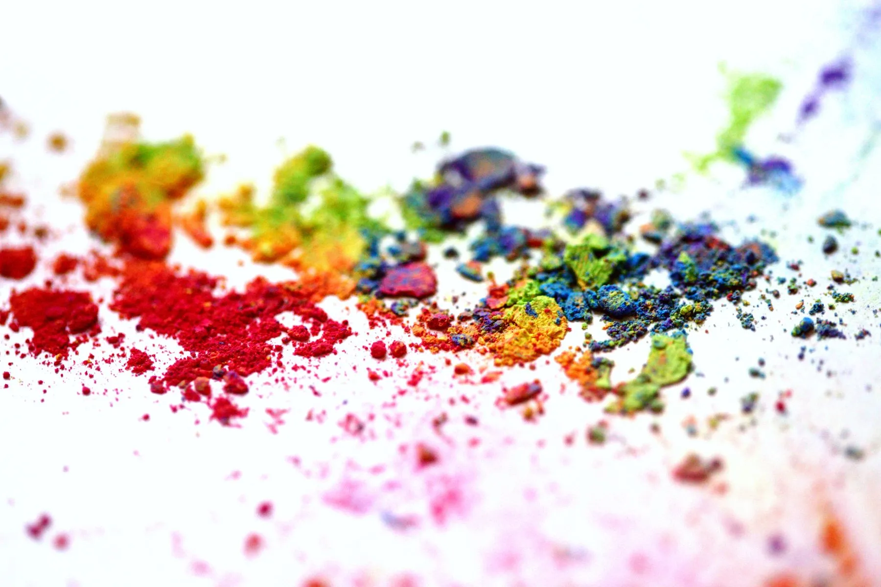 Loose pigment powders in red, orange, green and blue scattered across a white surface