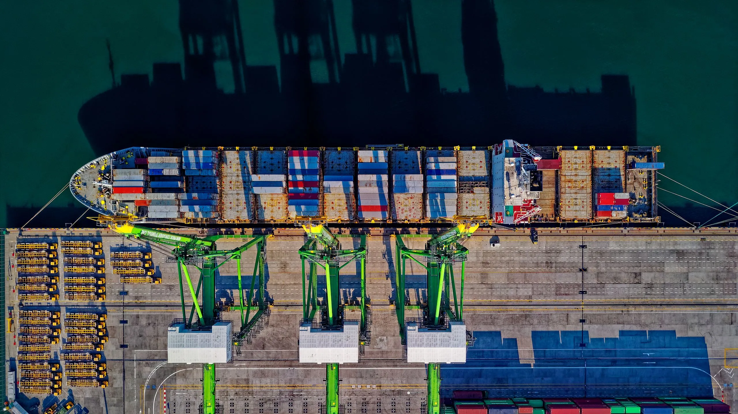 A container ship berthed beneath gantry cranes, seen from above