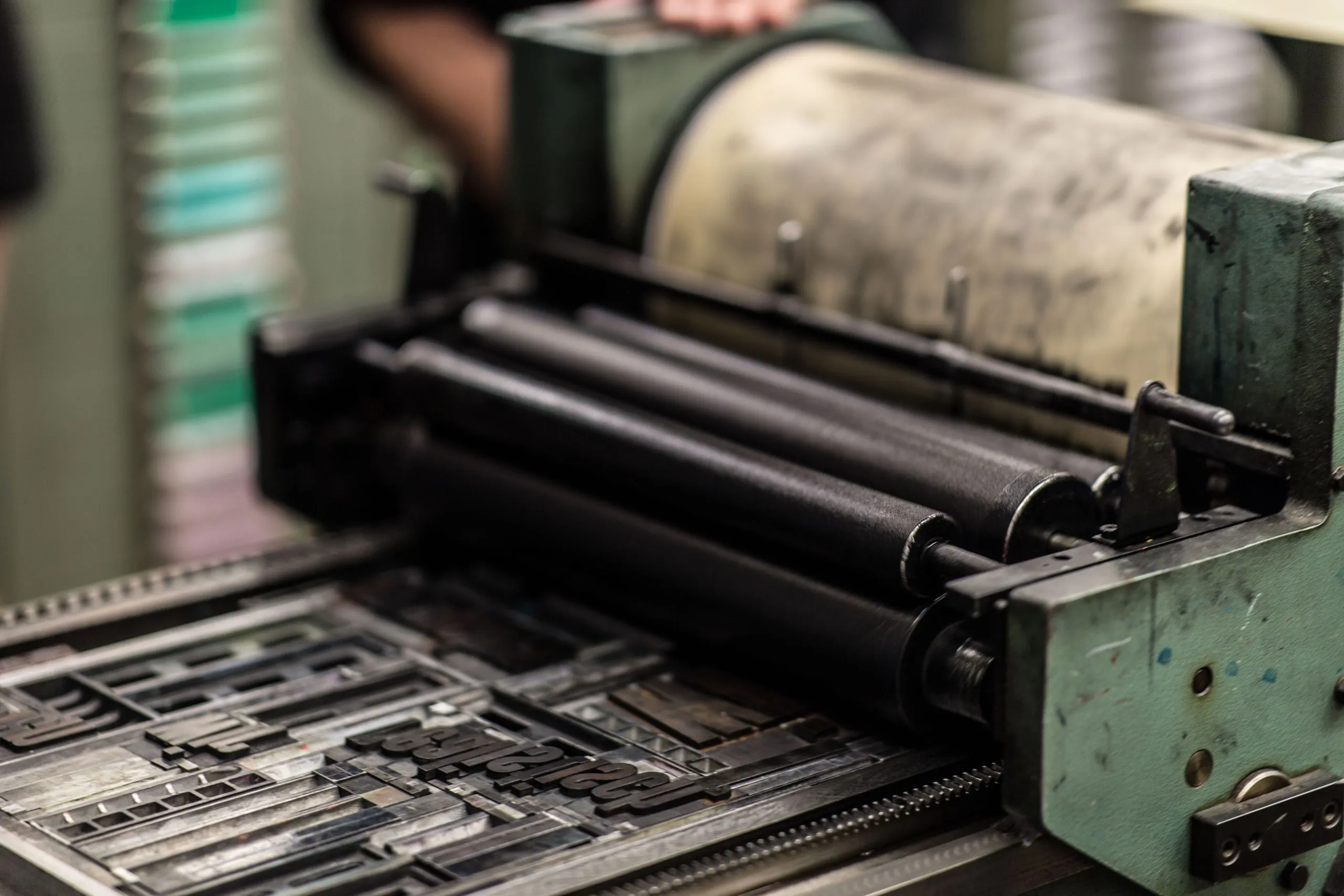 Inked rollers on a printing press, above a bed of metal type