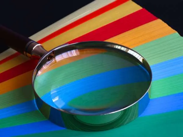 A magnifying glass over a fanned stack of coloured stock